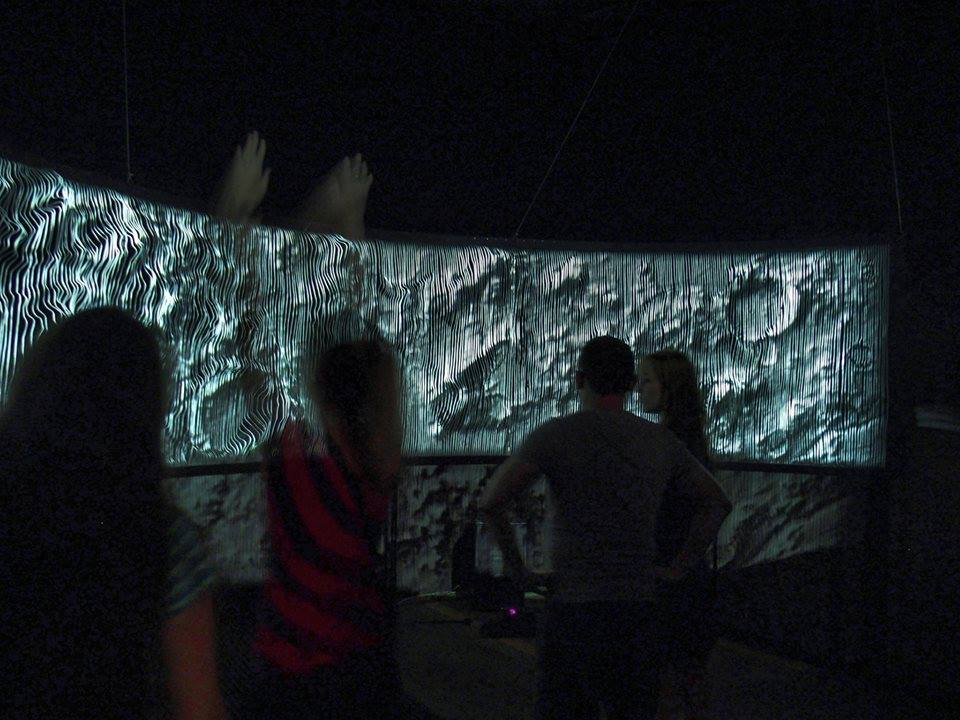 Visitors standing at the curved screen, two large hand outlines picked out in the projection.